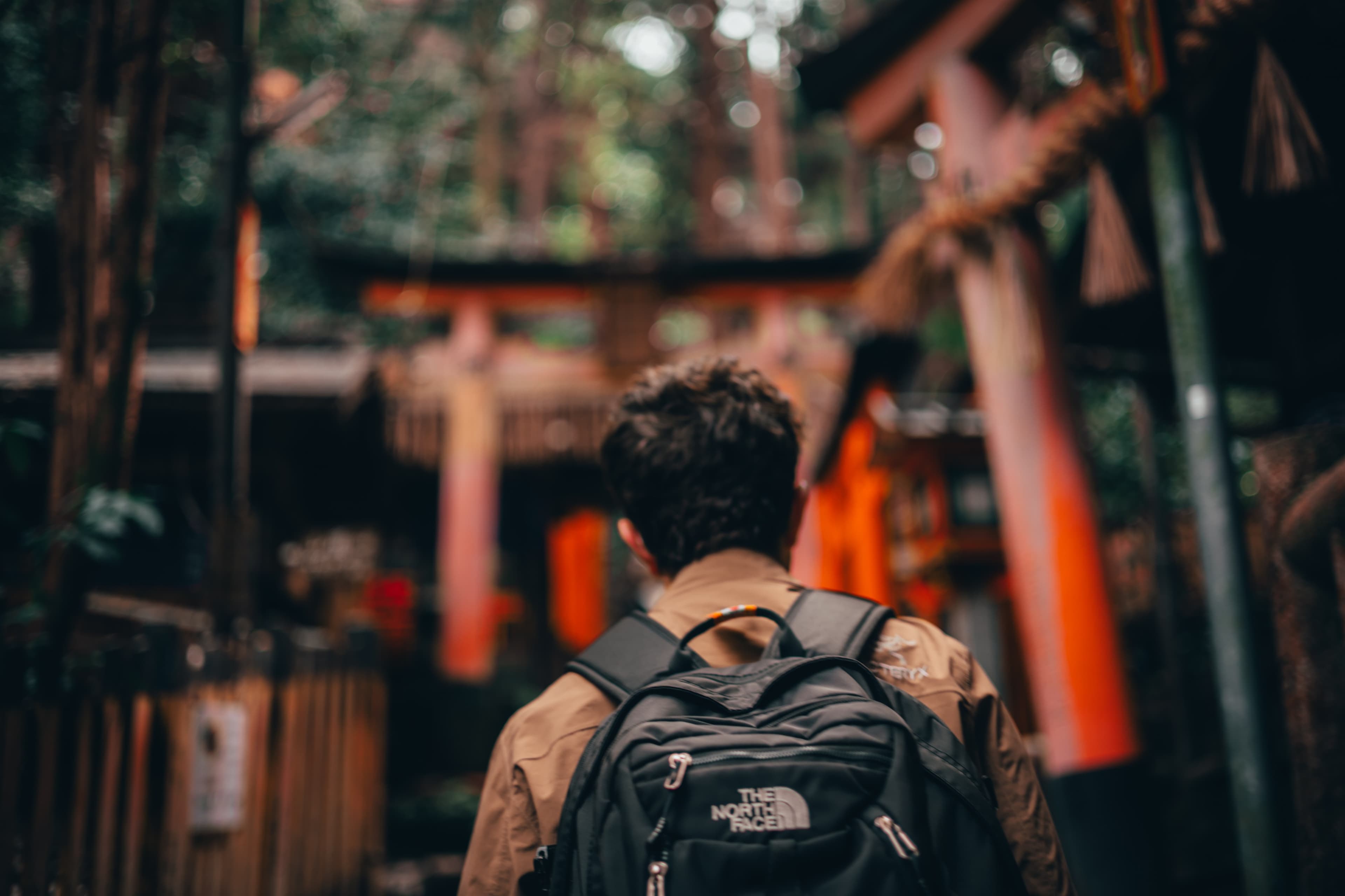Passing beneath a tunnel of red torii gates at Fushimi Inari, lanterns lighting the path ahead.