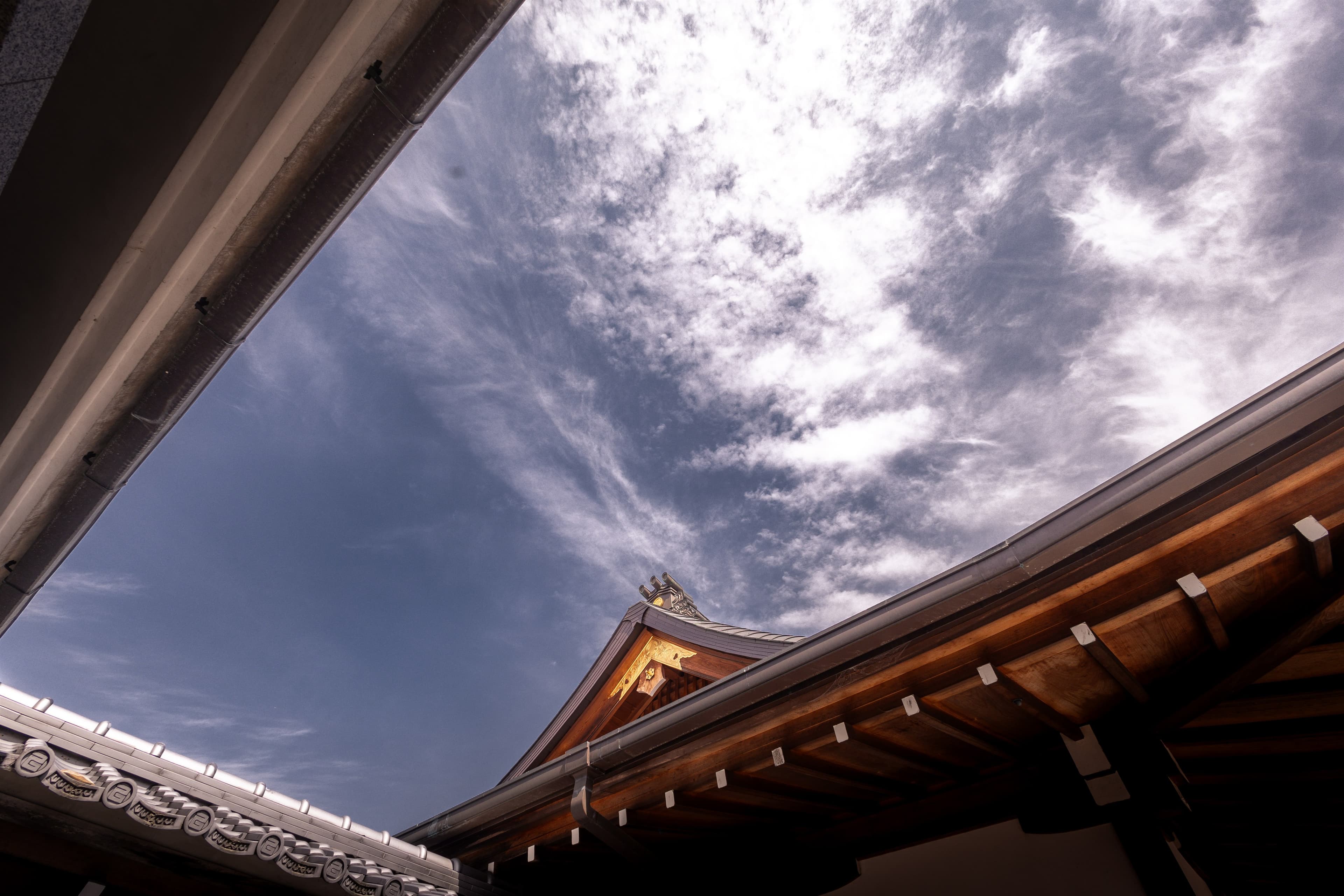 Looking up along a temple eave to a gilded roof ornament against streaked blue sky.