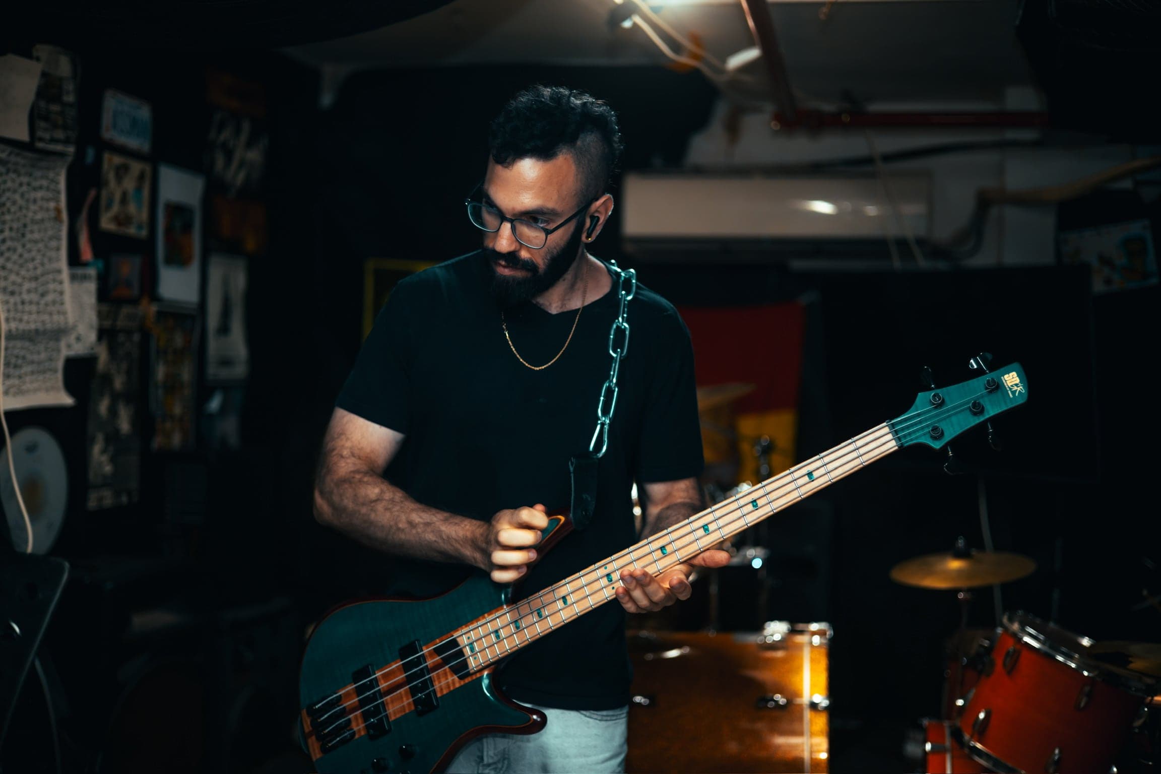 The bassist plays with his head down, a chain necklace catching the light against the fretboard of his bass.
