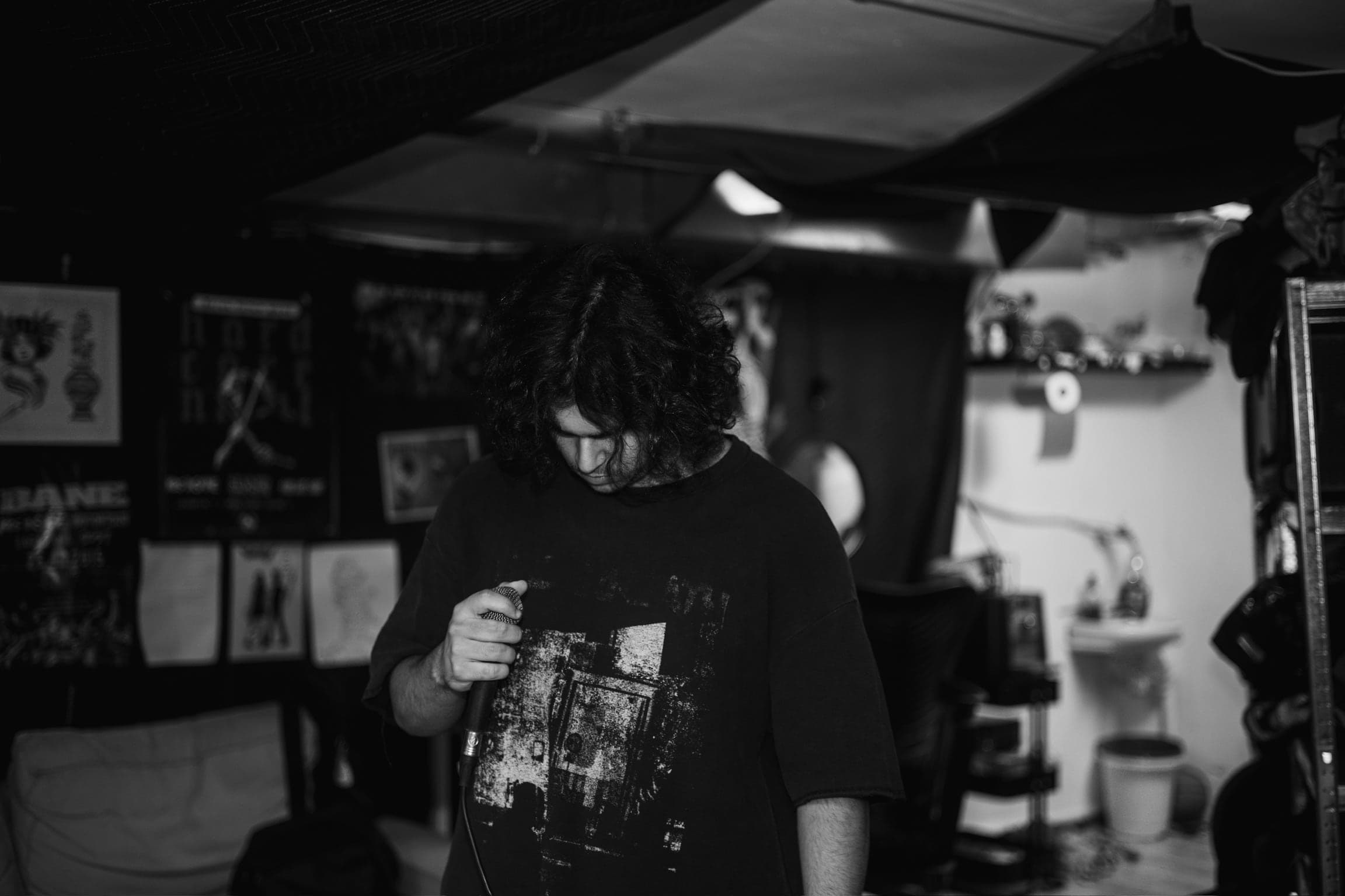 Black and white — the vocalist stands with his head down, hair covering his face, microphone held loosely at his side.