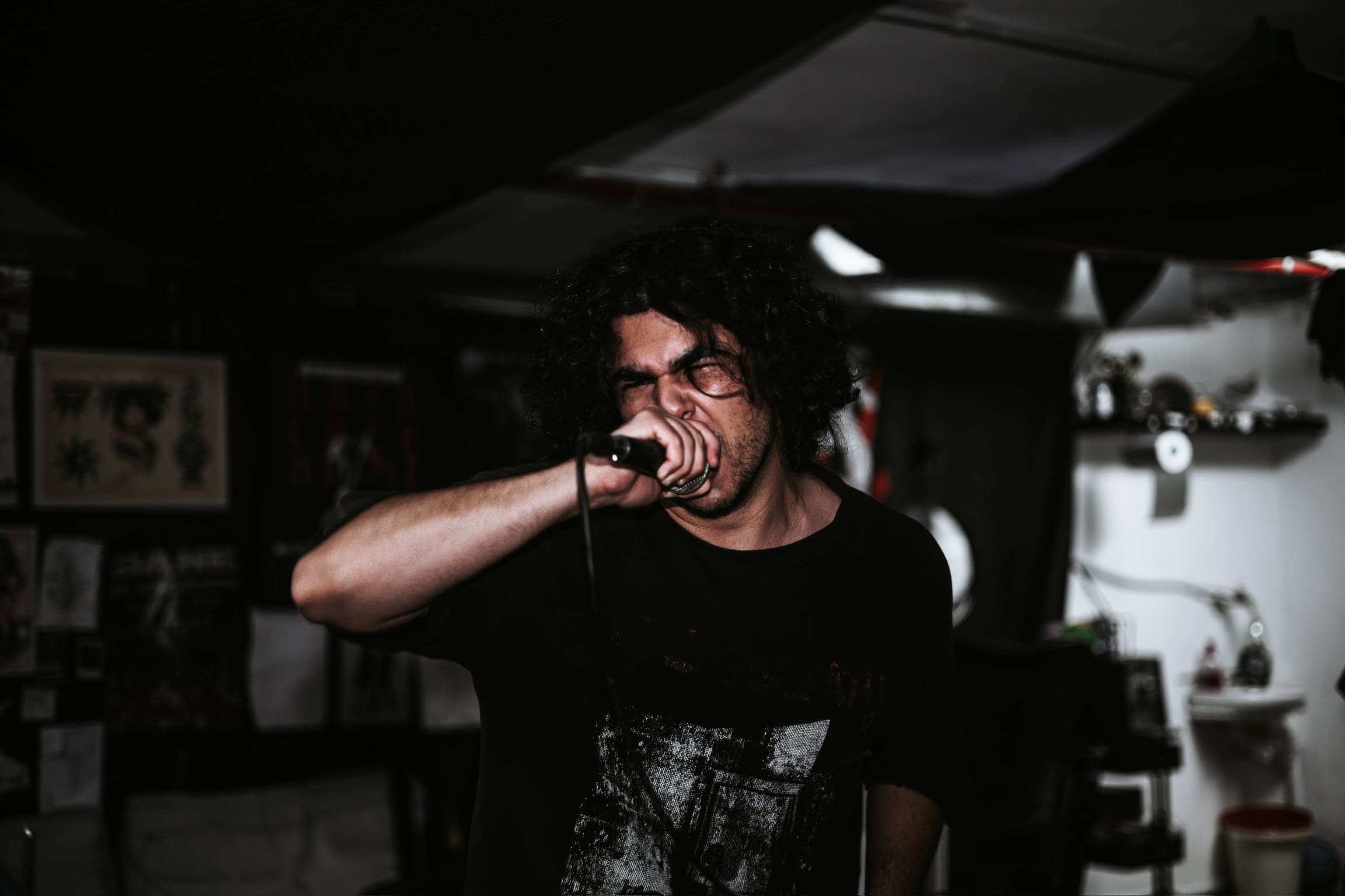 Black and white — the vocalist screams into the microphone, eyes shut, fist clenched around it.
