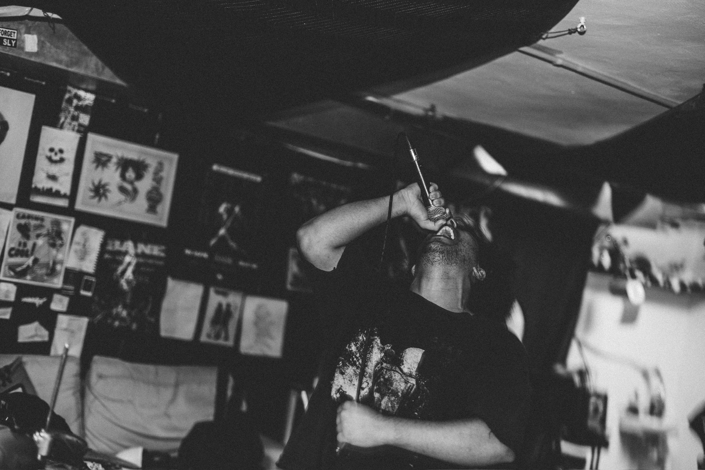 Black and white — the vocalist's head snaps back, microphone raised overhead, mid-scream.