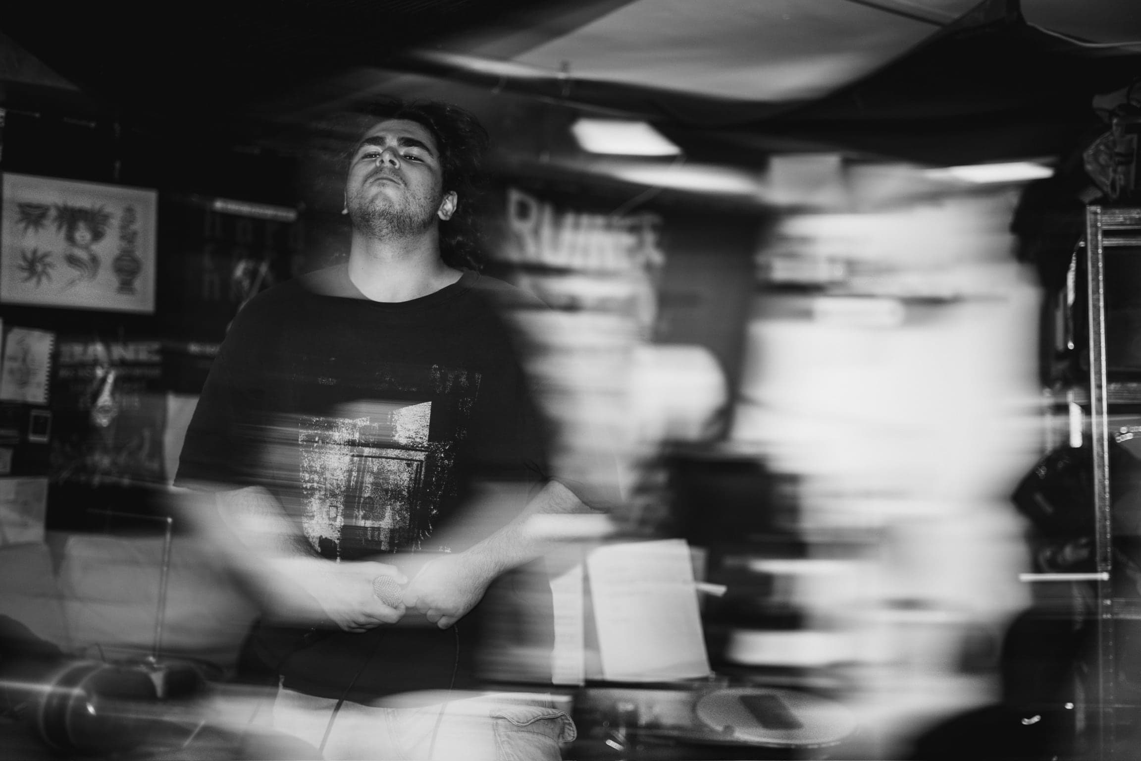 Black and white — a long exposure catches the vocalist between movements, the room streaking into blur around him.