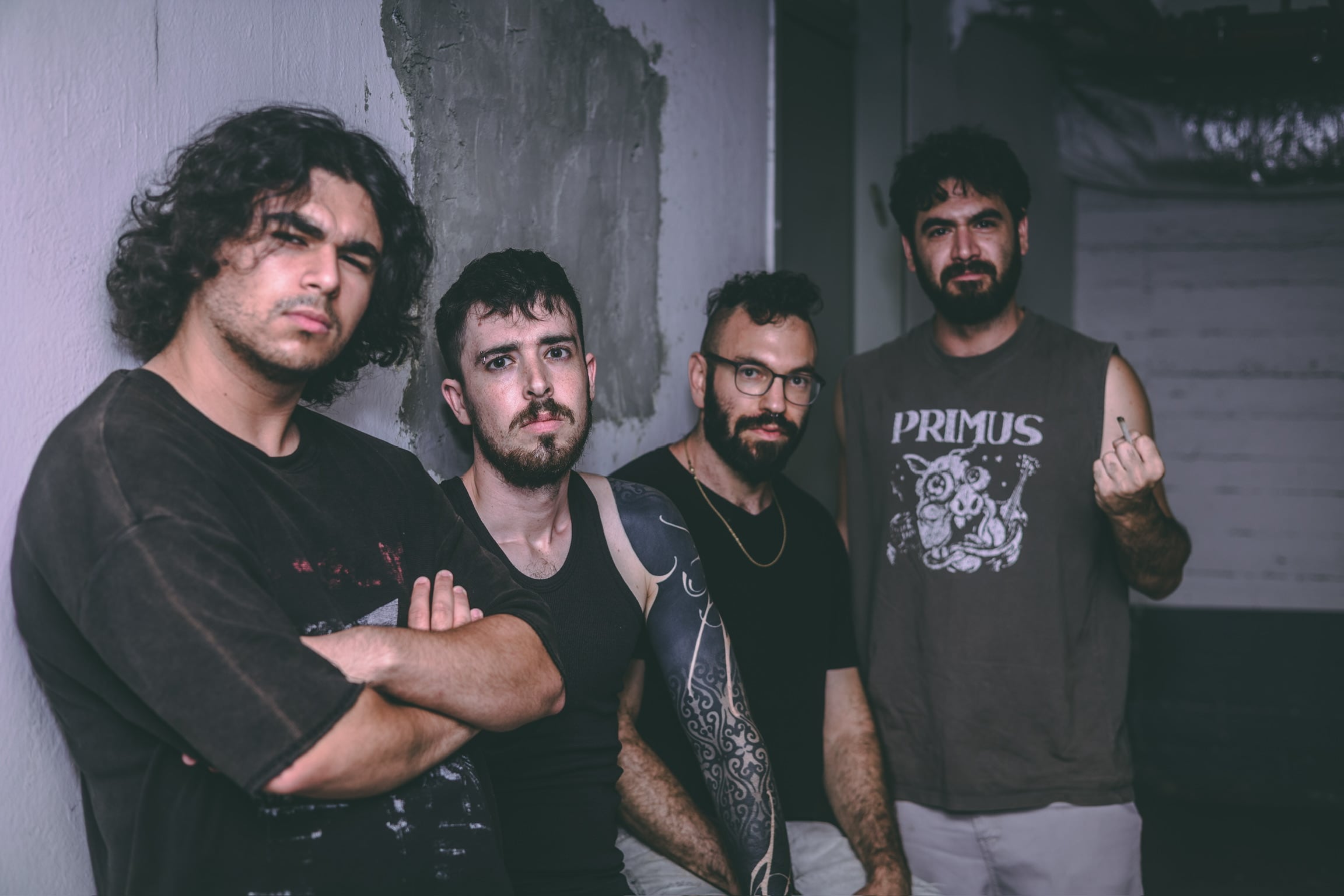The four members of Brand New Rebel stand shoulder to shoulder against a rough concrete wall, arms crossed, one member flipping off the camera.