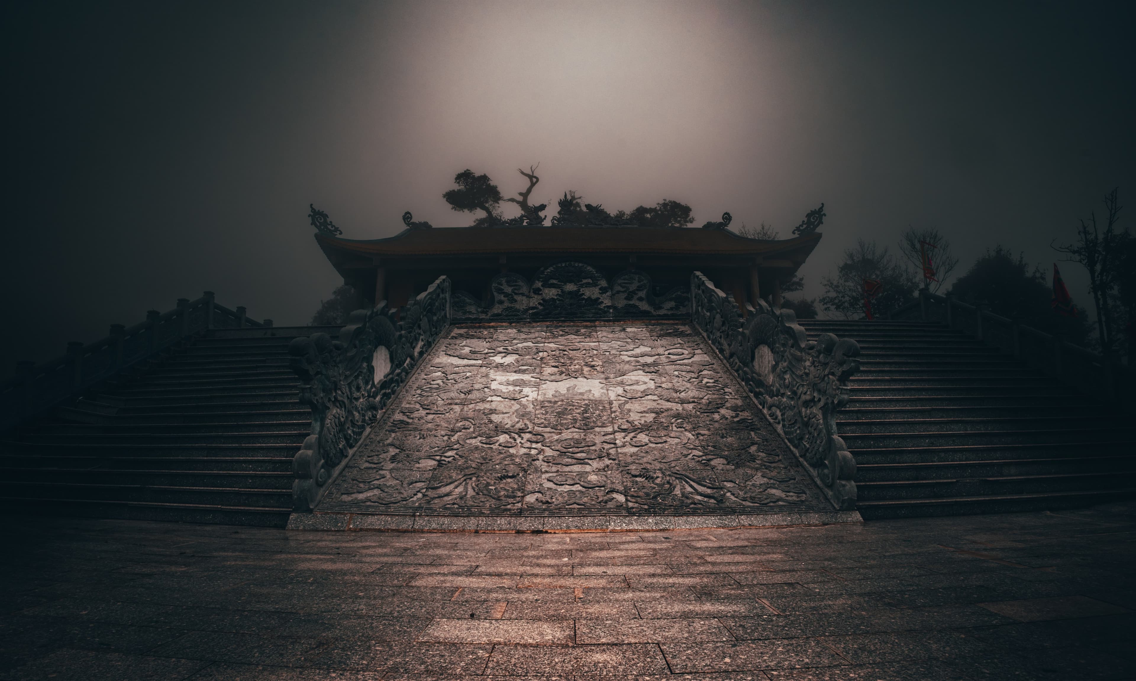 A dragon-carved stone stairway climbing to a hilltop pagoda, fog settling over the roofline at dawn.