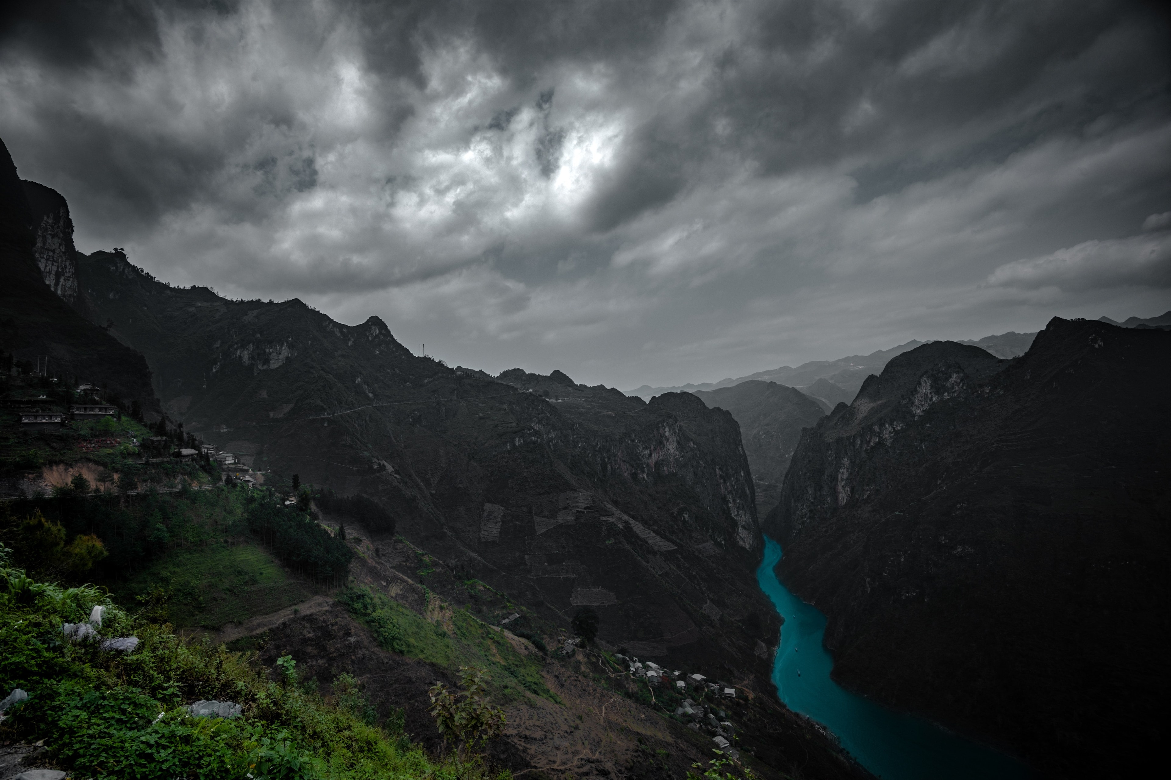 A turquoise river cutting through the Ha Giang mountains, terraced slopes falling away into shadow.