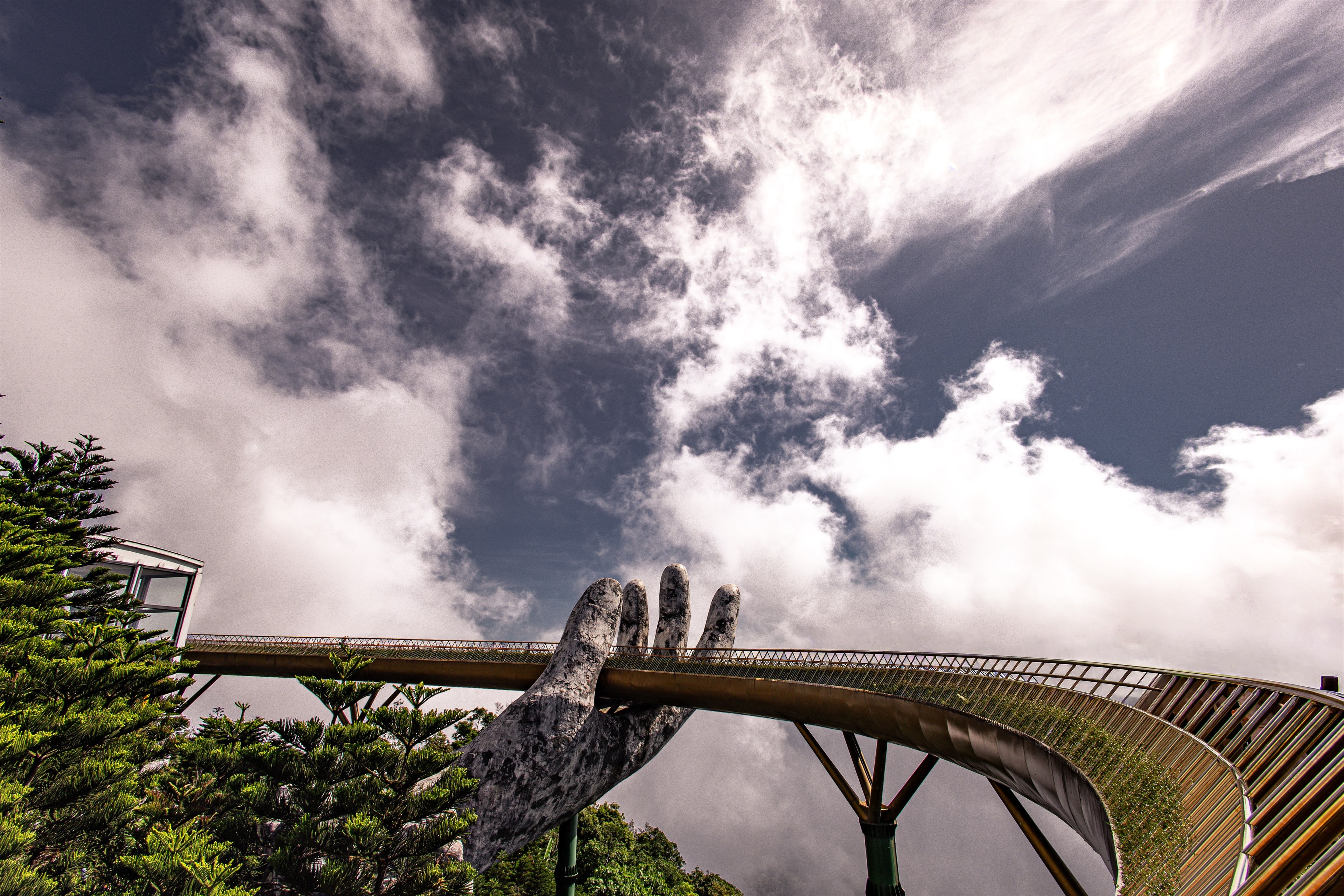Two giant stone hands cradle the Golden Bridge at Ba Na Hills, cloud rolling through the mountains behind it.